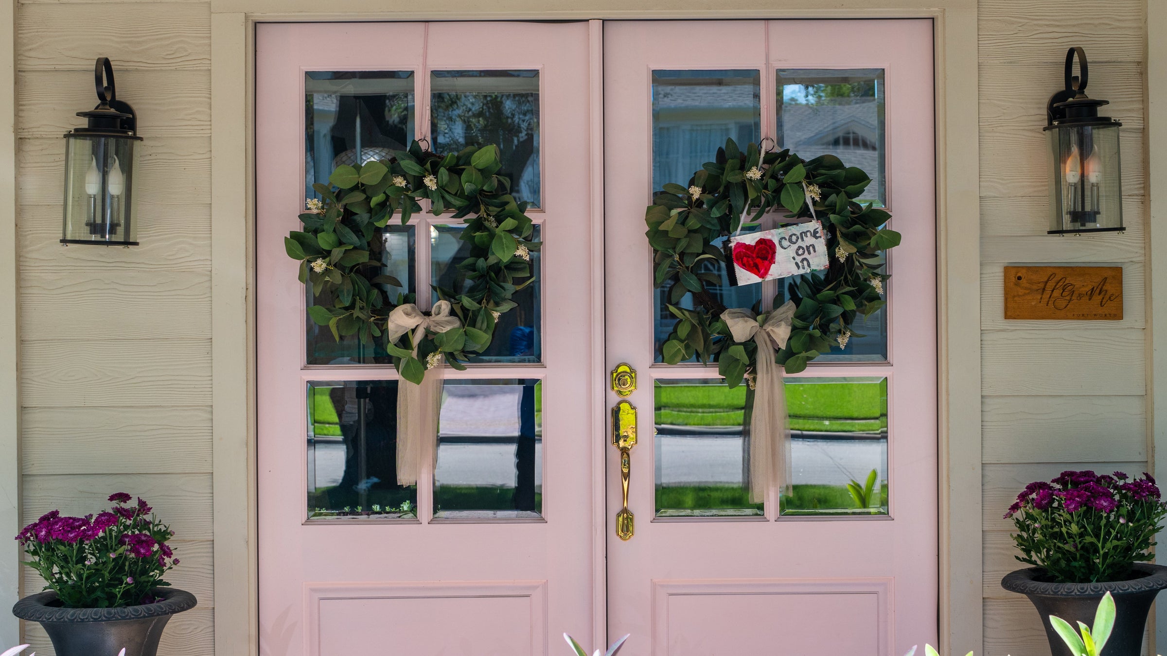 Pink front door with wreaths and decorative elements on a house exterior.